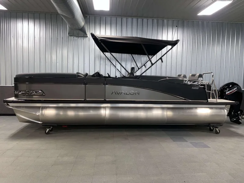 Slide: The Image of 2025 Avalon Catalina 2385 QLS Tritoon in showroom, sleek design, black canopy, metallic finish. - 19
