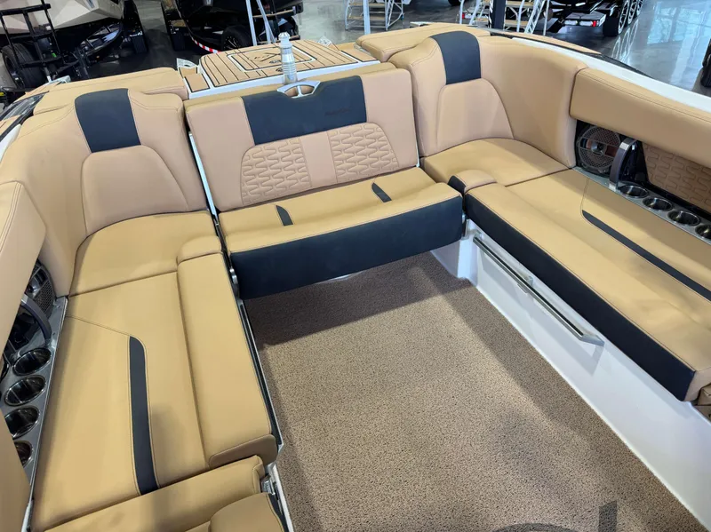 Slide: The Image of 2021 MasterCraft X24 boat interior with tan and black seating, cup holders, and carpeted flooring. - 18