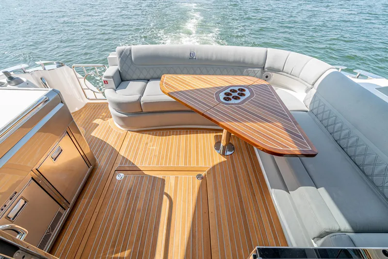 Slide: The Image of 2024 Riviera 4600 Sport Yacht deck with elegant seating and wooden table on open water. - 28