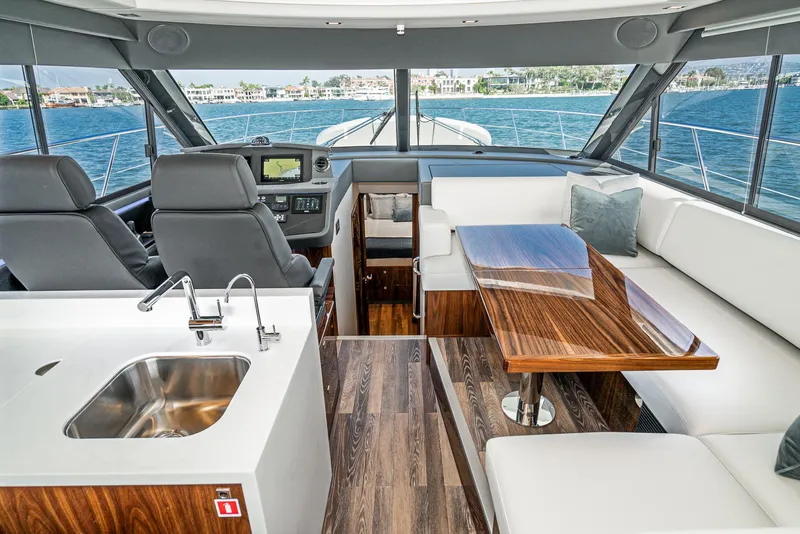 Slide: The Image of 2024 Riviera 4600 Sport Yacht interior with modern seating, wooden table, and sleek kitchen area. - 38