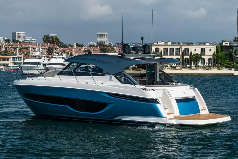 Slide: The Image of 2024 Riviera 4600 Sport Yacht cruising on a sunny day near luxury waterfront homes. - 5