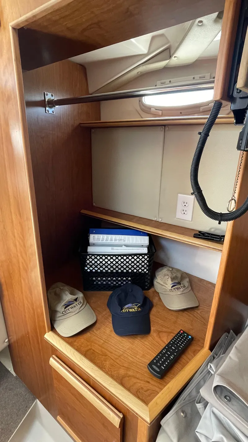 Slide: The Image of 2023 Cutwater C-288 interior storage with hats, remote, and organizer on wooden shelves. - 14