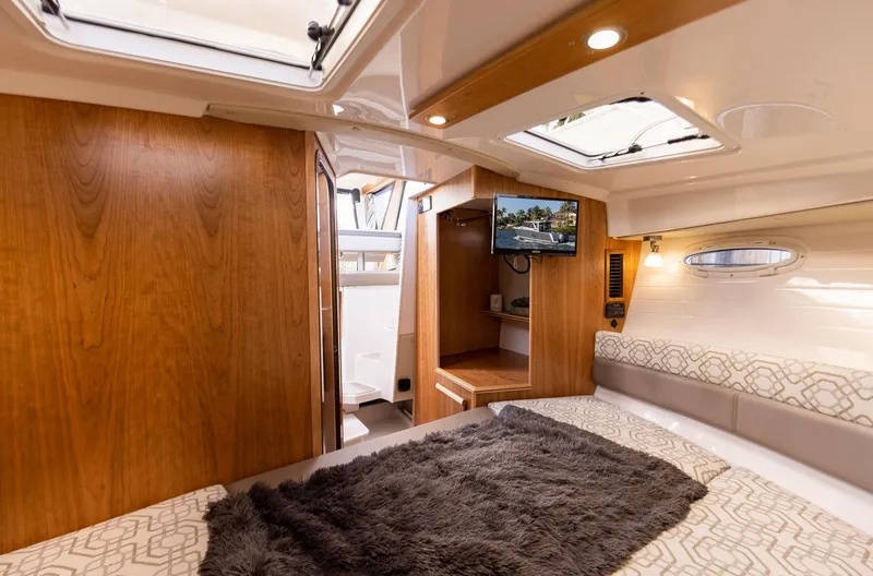 Slide: The Image of 2023 Cutwater C-288 interior cabin with cozy bedding, wood finish, and a mounted TV. - 32