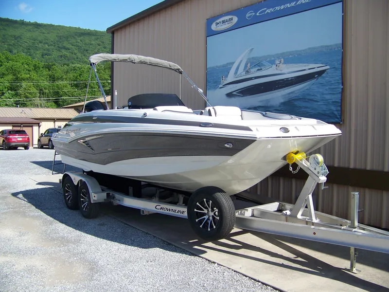 Slide: The Image of 2026 Crownline Eclipse E210 XS boat on trailer, parked outdoors near a building. - 2
