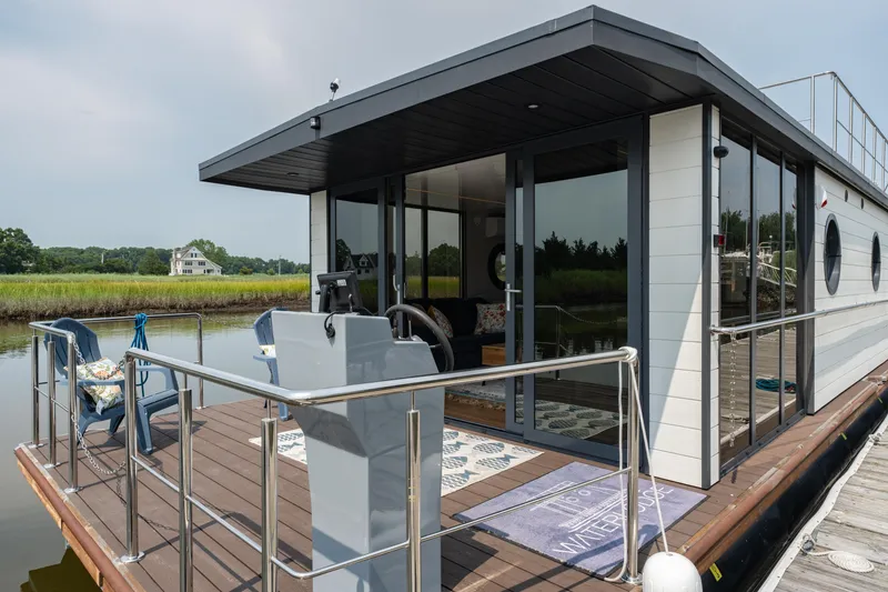 Slide: The Image of Modern Waterlodge Apart EL 2025 houseboat with glass doors, deck, and scenic waterway view. - 27