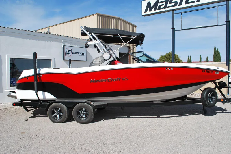 Slide: The Image of 2022 MasterCraft NXT24 boat in red and white on a trailer, parked outside a building. - 0