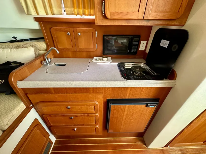 Slide: The Image of 2005 Stamas 320 Express boat kitchen with wood cabinets, sink, stove, microwave, and mini-fridge. - 34