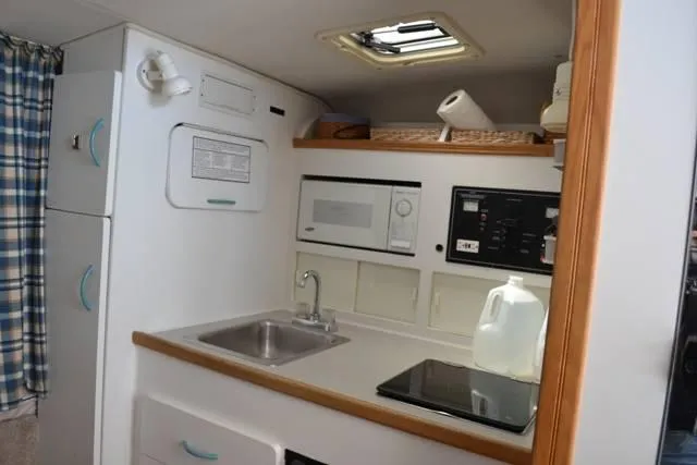 Slide: The Image of Compact kitchen area in a 1998 Rinker Fiesta Vee 280EC boat, featuring a sink, microwave, and stove. - 11