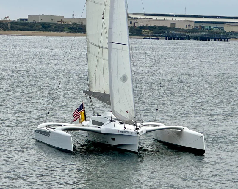 Slide: The Image of 2021 Dragonfly 25 Touring trimaran sailing on calm waters near industrial shoreline. - 5