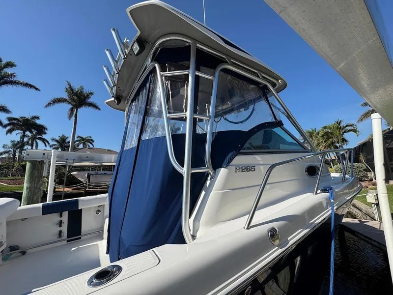 Slide: The Image of 2012 Robalo R265 Walkaround boat docked, featuring sleek design and blue canopy. - 3