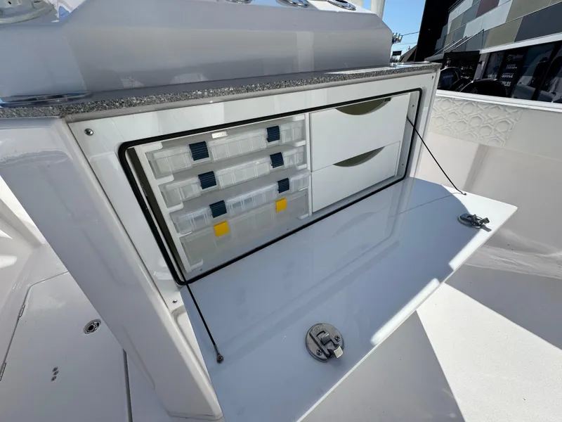 Slide: The Image of 2025 Aquasport 28AS Center Console storage compartment with organized tackle boxes and drawers. - 10