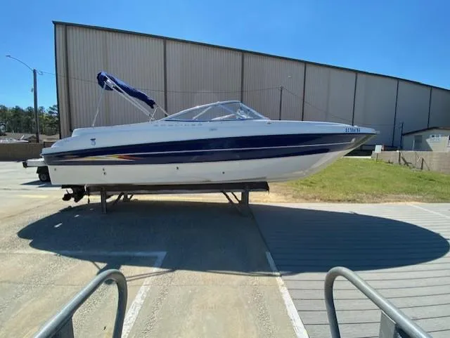The Image of 2005 Bayliner 249 SD boat on trailer, parked outdoors near a large building. - 1
