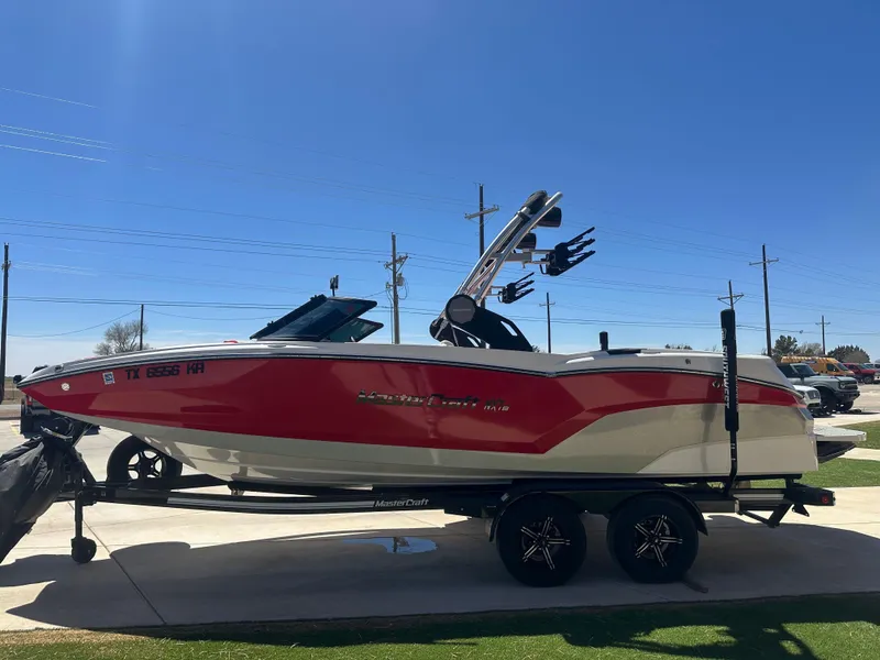 Slide: The Image of 2023 MasterCraft NXT22 boat in red and white on a trailer, parked outdoors. - 4