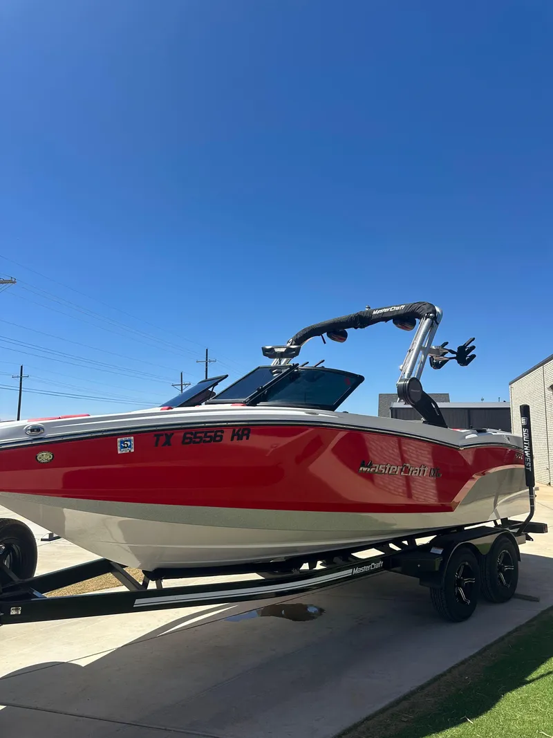 Slide: The Image of 2023 MasterCraft NXT22 boat in red and white on a trailer under clear blue sky. - 5