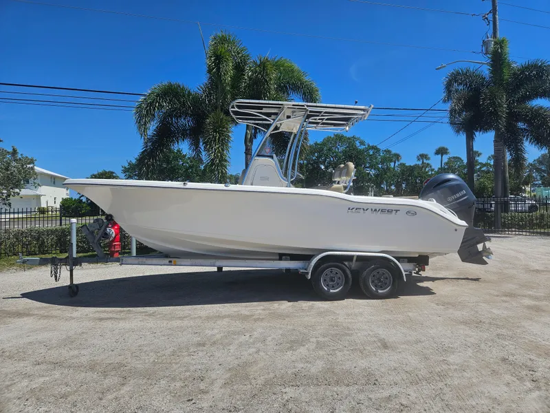 Slide: The Image of 2018 Key West 219 FS boat on trailer, parked outdoors with palm trees in background. - 2