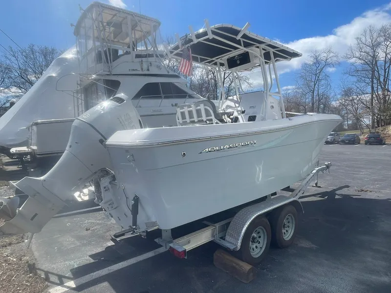 Slide: The Image of 2022 Aquasport 2100 CC boat on trailer, parked outdoors under a clear blue sky. - 10