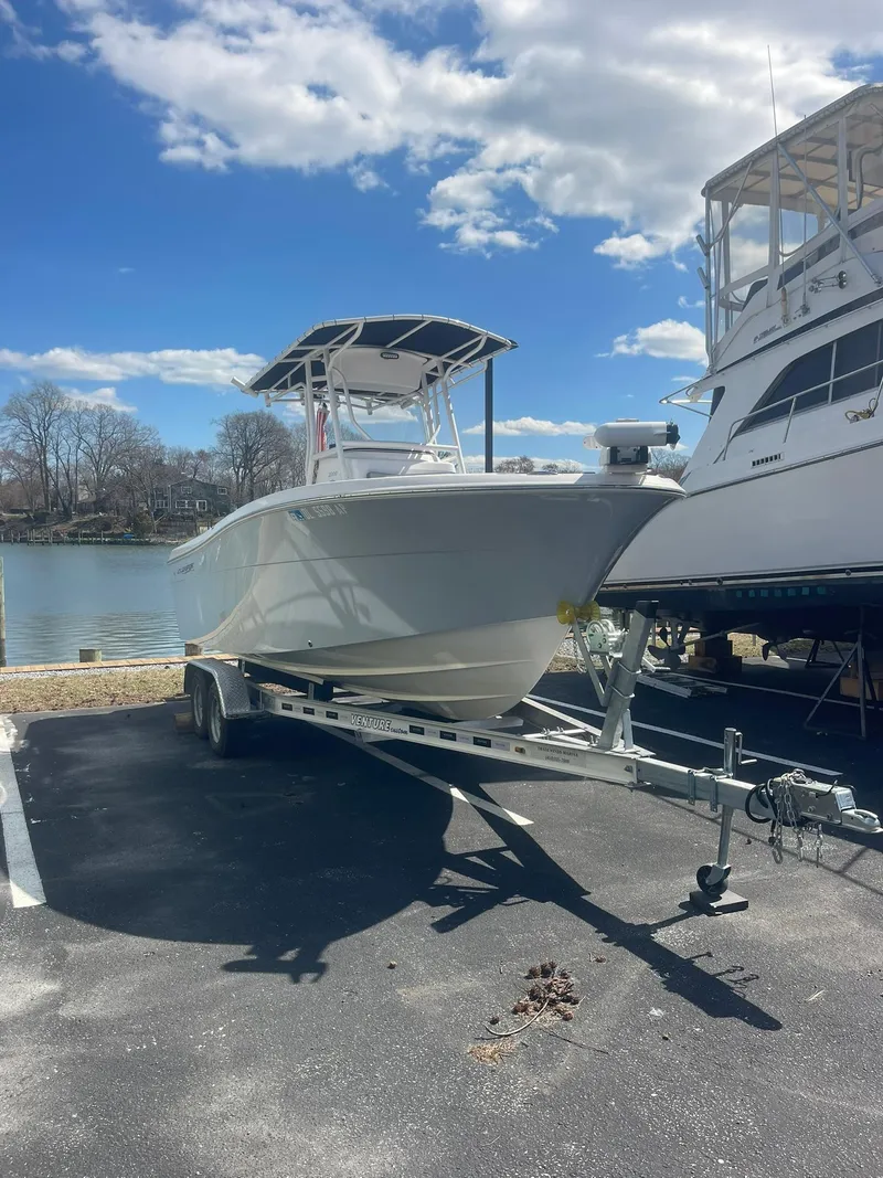 Slide: The Image of 2022 Aquasport 2100 CC boat on trailer, parked near water under a blue sky. - 26
