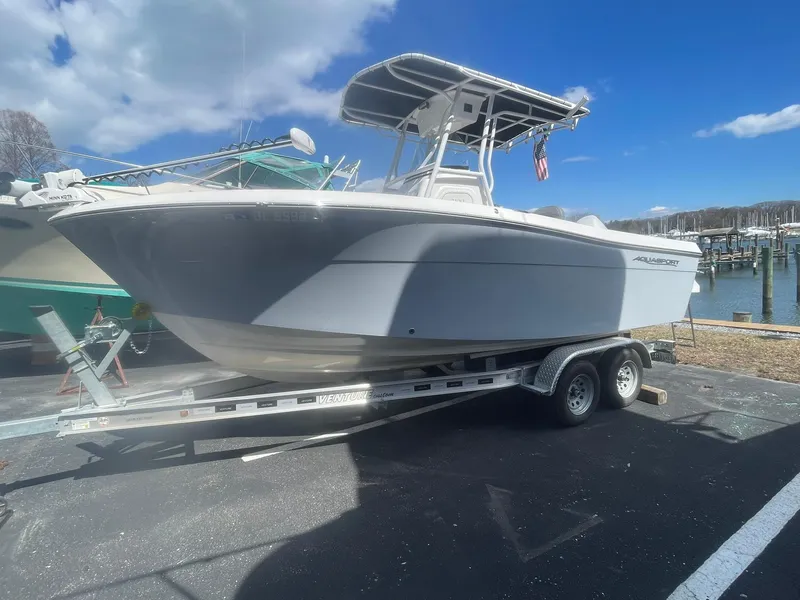 Slide: The Image of 2022 Aquasport 2100 CC boat on trailer, parked outdoors under a blue sky. - 5