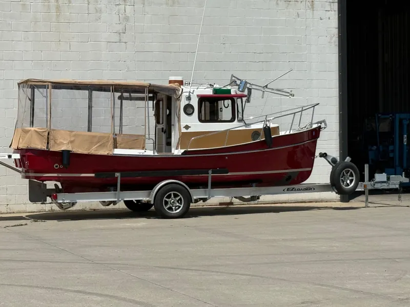 Slide: The Image of 2016 Ranger Tugs R-21 EC boat on trailer, red hull, parked by a white brick wall. - 3