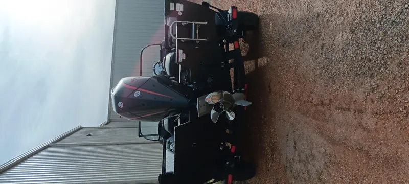 Slide: The Image of 2024 Ranger VX1888 WT boat with powerful outboard motor, parked on gravel near a building. - 24