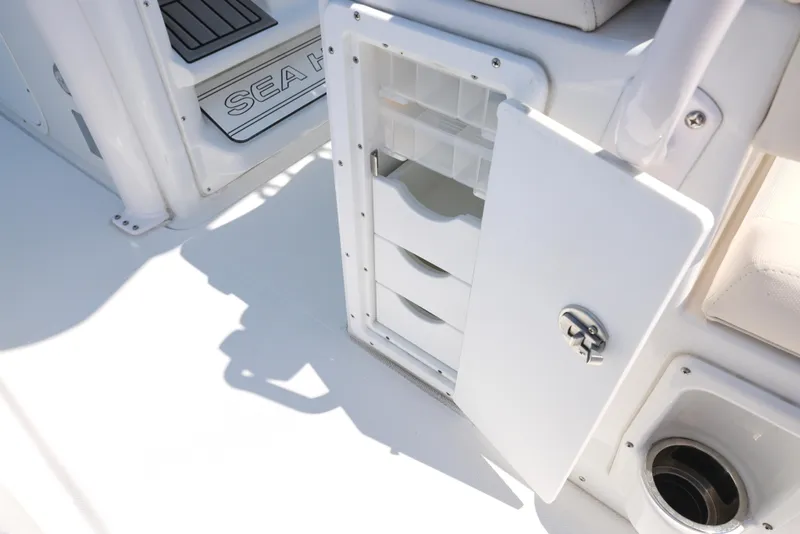 Slide: The Image of 2025 Sea Hunt Ultra 265 SE boat storage compartment with open door and visible drawers. - 12