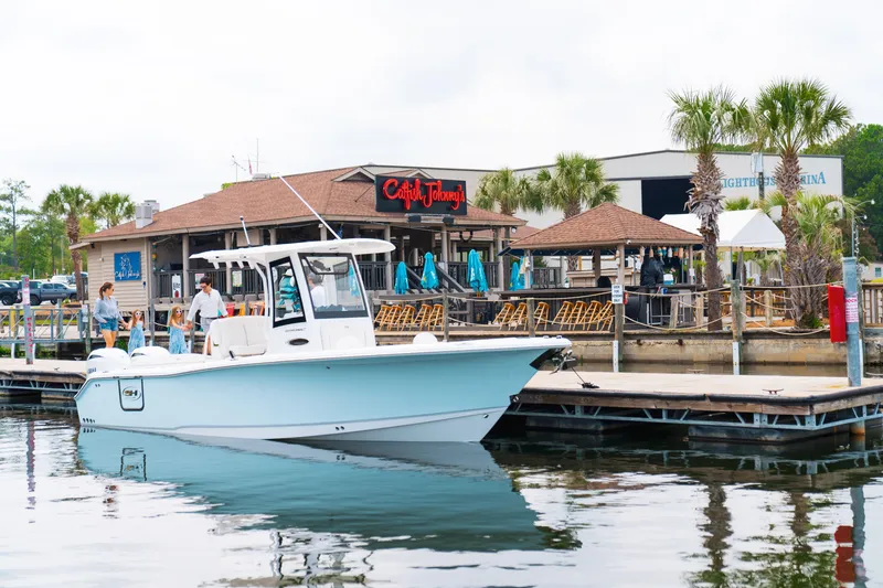 Slide: The Image of 2025 Sea Hunt Ultra 265 SE boat docked near waterfront restaurant and marina. - 23