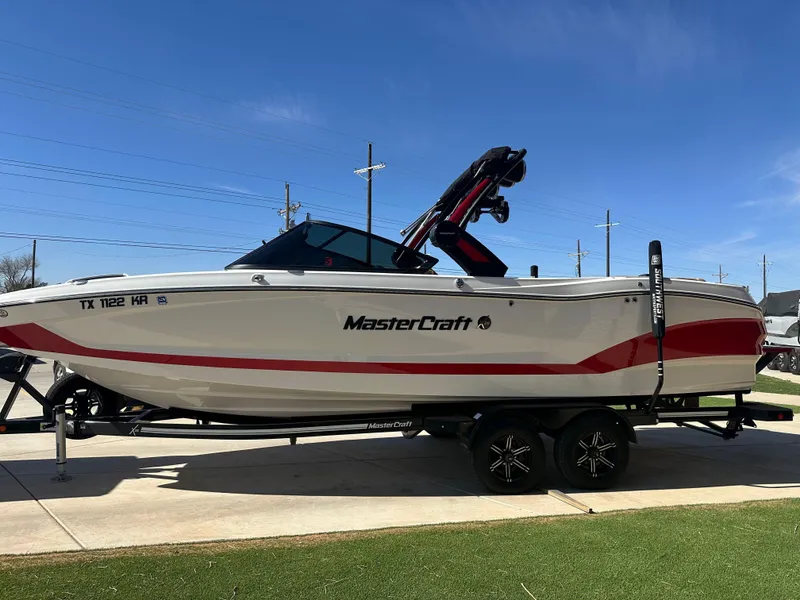 Slide: The Image of 2023 MasterCraft X26 boat on trailer, white with red accents, parked outdoors. - 3