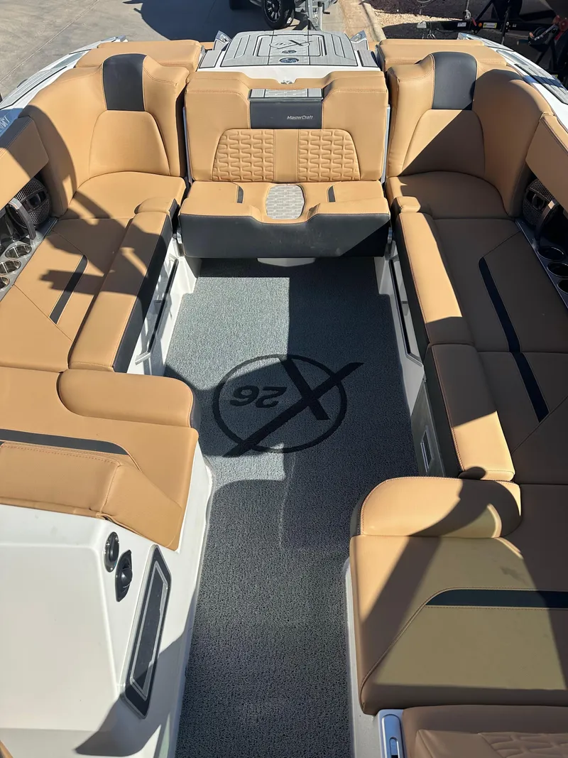 Slide: The Image of 2023 MasterCraft X26 boat interior with tan seating and logo on gray flooring. - 8