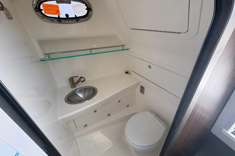 Slide: The Image of 2026 Boston Whaler 285 Conquest bathroom with sink, toilet, and porthole window. - 19