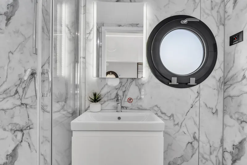 Slide: The Image of Modern bathroom with marble walls, round window, and sleek vanity in Waterlodge Apart XXL 2025. - 31