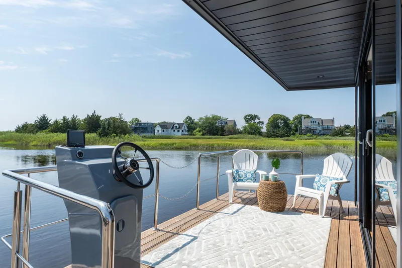 Slide: The Image of Modern Waterlodge Apart XXL houseboat deck with chairs, steering wheel, and scenic waterfront view. - 5
