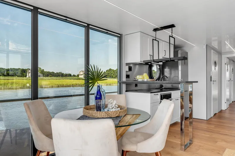 Slide: The Image of Modern Waterlodge Apart XXL 2025 interior with dining area, large windows, and scenic water view. - 7