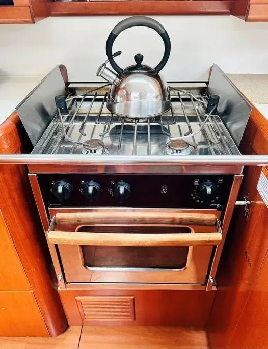 Slide: The Image of 2007 Beneteau 49' Cruiser kitchen with stove and kettle, featuring wooden cabinetry. - 23
