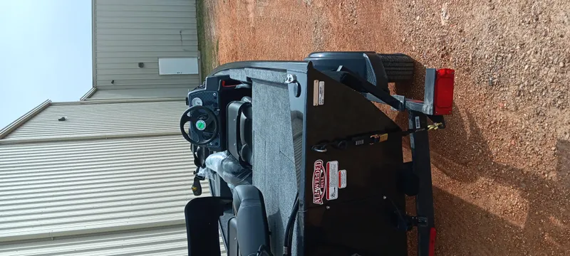 Slide: The Image of 2025 Tracker Bass Tracker Classic XL boat on a trailer, parked on gravel near a metal building. - 14