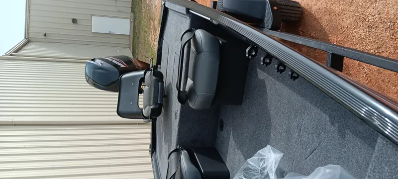 Slide: The Image of 2025 Tracker Bass Tracker Classic XL boat interior with seating and motor, parked outdoors. - 28