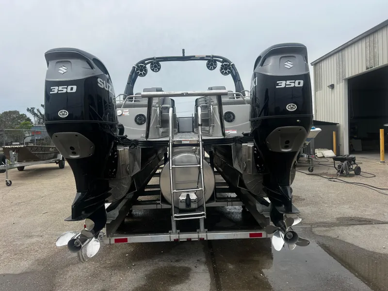 Slide: The Image of 2022 Manitou 27 boat with dual Suzuki 350 engines, parked outdoors near a warehouse. - 12