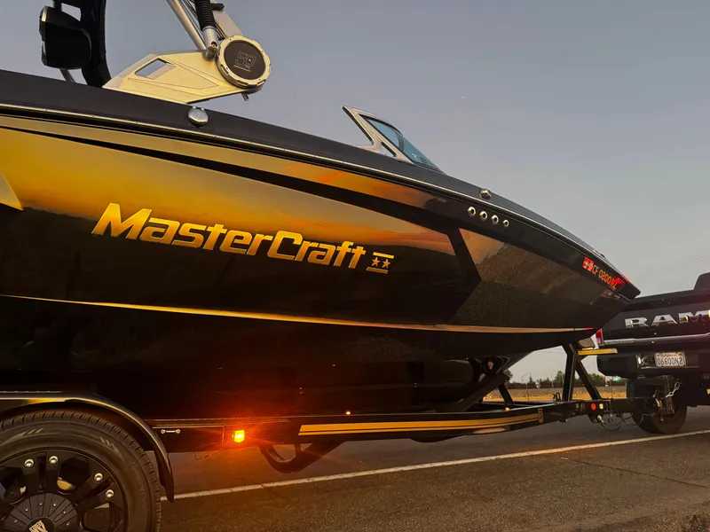 Slide: The Image of 2018 MasterCraft XStar boat on trailer at sunset, showcasing sleek design and branding. - 1