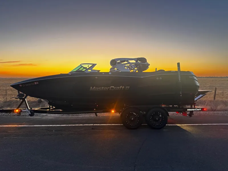 Slide: The Image of 2018 MasterCraft XStar boat on trailer at sunset, showcasing sleek design and silhouette. - 14