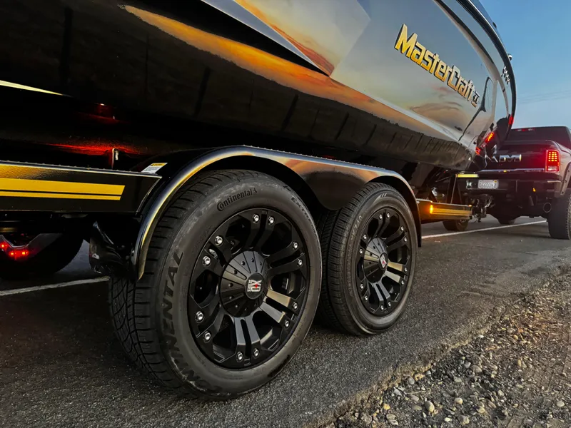 Slide: The Image of 2018 MasterCraft XStar boat trailer with black wheels, parked on a road at sunset. - 6