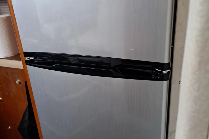 Slide: The Image of 1999 Cruisers aft cabin refrigerator with sleek black handle in a wooden interior setting. - 14