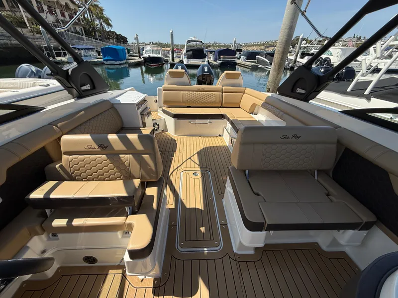 Slide: The Image of 2022 Sea Ray 290 SDX OB boat interior with tan seating and wood flooring at marina. - 19