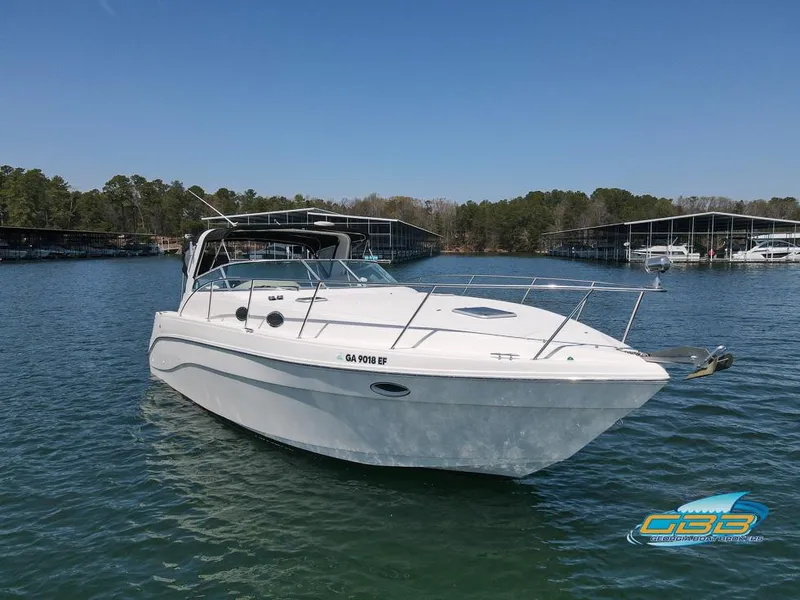Slide: The Image of 2000 Rinker 340 Express Cruiser on a serene lake with marina backdrop. - 7