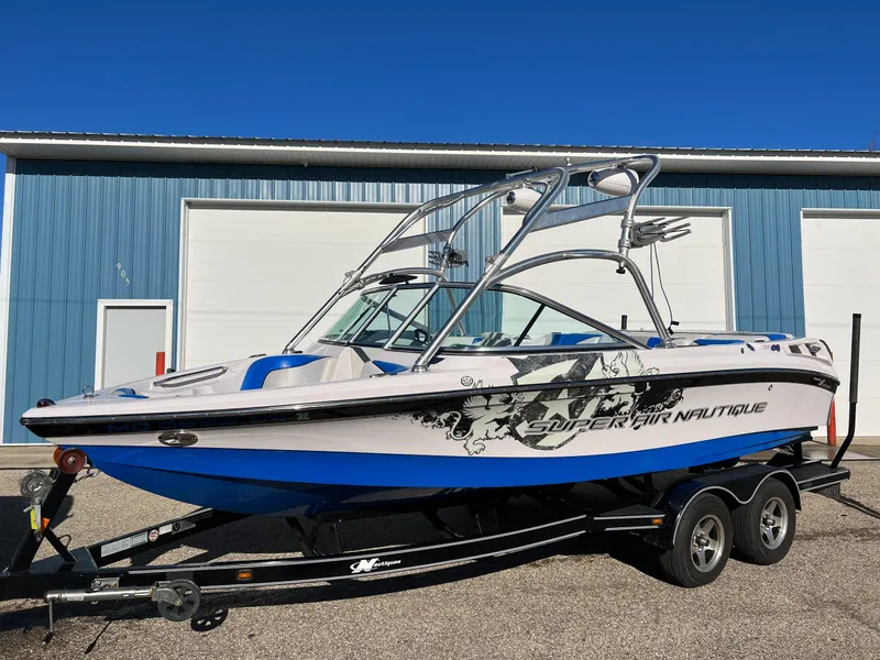 Slide: The Image of 2008 Nautique 210 boat on trailer, blue and white design, parked outside a blue building. - 11