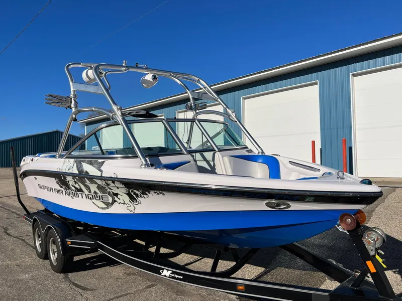 Slide: The Image of 2008 Nautique 210 boat on trailer, parked near blue warehouse. - 3