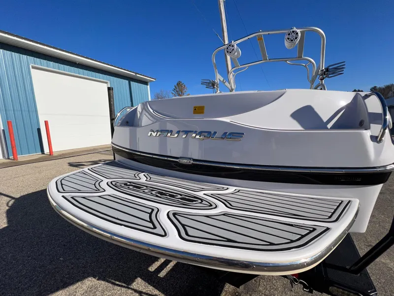Slide: The Image of 2008 Nautique 210 boat with swim platform, parked near a blue building under clear skies. - 7