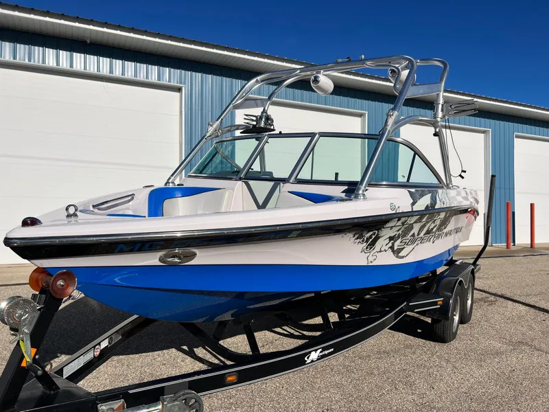 Slide: The Image of 2008 Nautique Super Air 210 boat on trailer, blue and white design, parked near a building. - 8