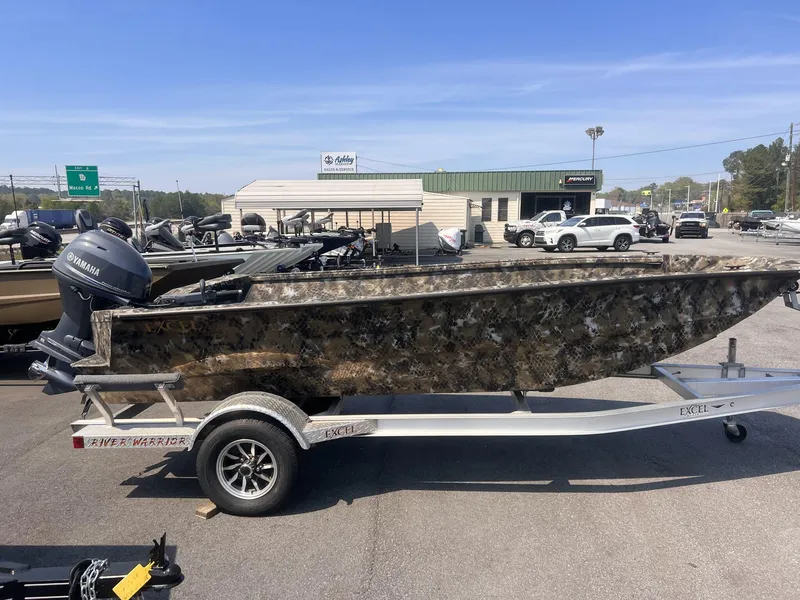 Slide: The Image of 2024 Excel RIVER WARRIOR 1651 boat on trailer, camo design, outdoor dealership setting. - 1