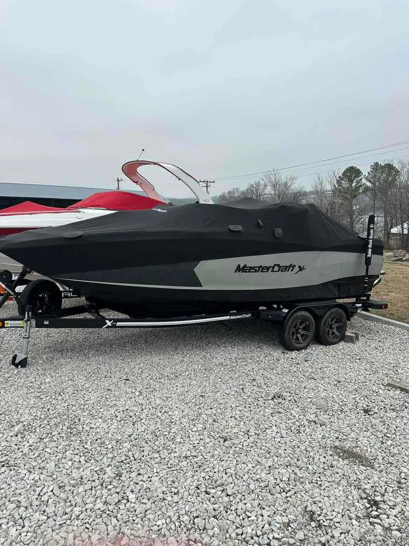 Slide: The Image of 2020 MasterCraft XStar boat covered on a trailer, parked on gravel. - 2