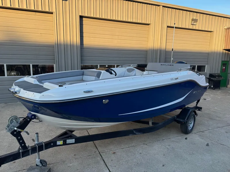 Slide: The Image of 2025 Bayliner D20 boat on trailer, blue and white, parked outside a garage. - 1
