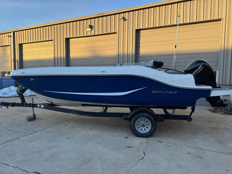 Slide: The Image of 2025 Bayliner D20 boat on trailer, parked outside industrial building. - 2